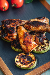 Grilled chicken wings with tomatoes, zucchini and peppers on a stone platter 