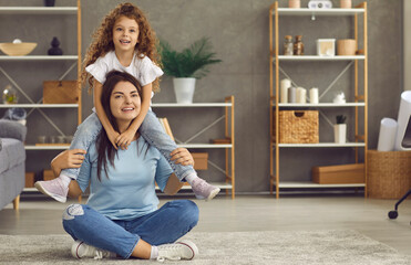 Happy single mom and her child playing at home. Portrait of positive cheerful smiley mother and cute sweet little daughter sitting on rug in stylish living room with underfloor heating. Family concept