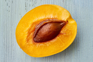 Half of a yellow ripe apricot with a bone on a blue table
