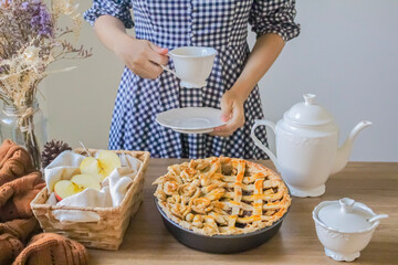 Decorated apple pie on a wooden table and a tea pot and cup of tea. Afternoon tea concept.