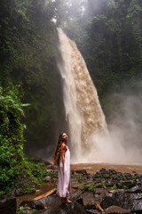 Naklejka premium Beautiful woman in a pink dress near a waterfall in Bali