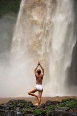 Beautiful woman doing yoga near a waterfall in Bali