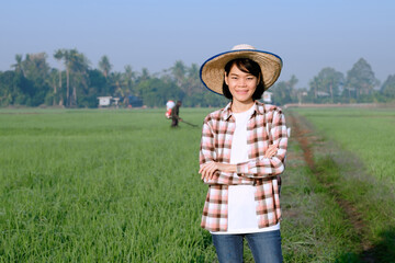 A female farmer wearing a striped shirt poses with her arms crossed and a smiling face in a field.