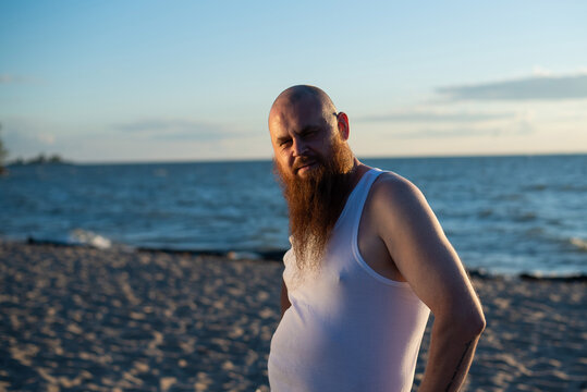 A humorous portrait of a brutal man in a T-shirt and boxers on the beach at sunset