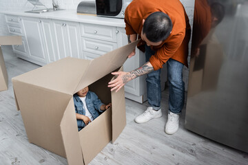 asian man looking at daughter hiding in carton box
