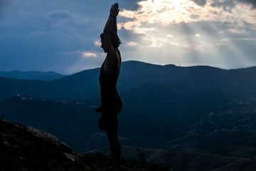 silhouette of a woman in the rays of the sunset against the background of the mountains is engaged in yoga,  shooting from the side, the general plan, in the air