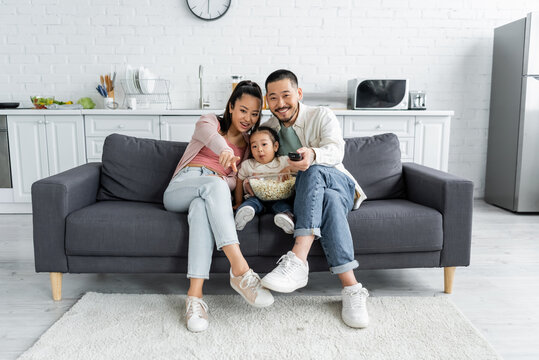 Joyful Asian Family Watching Movie With Bowl Of Popcorn In Living Room