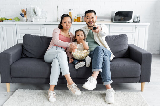 Asian Family Watching Tv And Eating Popcorn In Living Room