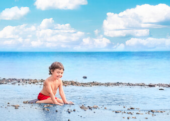 little child sitting in the sea with pebbles