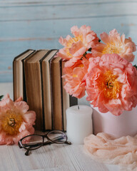 Vintage books, candles, glasses and pink peach peony bouquet  on a light blue background, soft selective focus