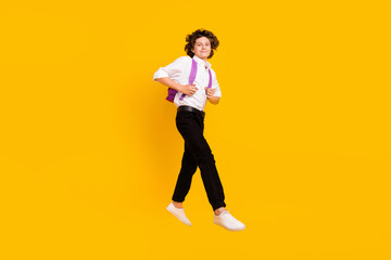 Fototapeta na wymiar Full length photo of funny small brunet boy jump wear bag uniform shoes isolated on yellow background