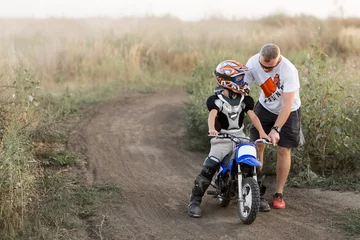 Kid on a motorcycle doing motocross. A little boy learns to ride a motorbike. The coach teaches the child to drive a motorcycle. Son and father on the track. © Aleksandr