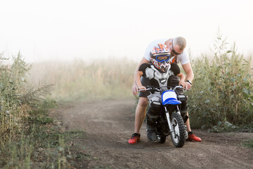 Kid on a motorcycle doing motocross. A little boy learns to ride a motorbike. The coach teaches the...