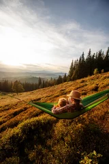 Foto op Plexiglas Jongenstoerist die in een hangmat in de bergen bij zonsondergang rusten © Maygutyak