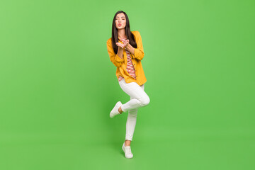 Fototapeta na wymiar Photo of dreamy adorable young woman dressed casual clothes sending you air kiss walking isolated green color background