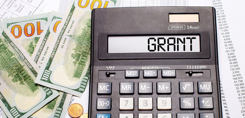 Against the background of cash and documents is a black calculator with the text GRANT on the scoreboard. Business concept