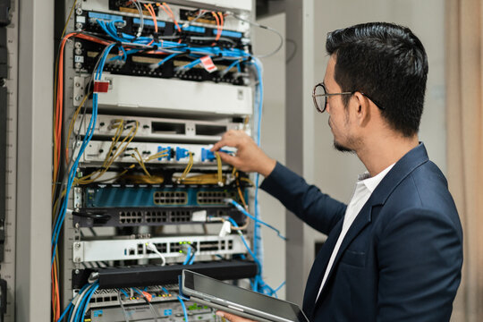 Stock photo of a young network technician holding tablet working to connecting network cables in server cabinet in network server room. IT engineer working in network server room