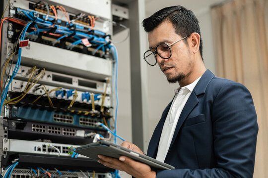 Stock photo of a young network technician holding tablet working to connecting network cables in server cabinet in network server room. IT engineer working in network server room