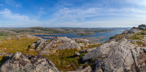 Fototapeta na wymiar Wide panorama view from above of a rock cliff and the ocean and islands on the horizon under blue sky. Norway. Valoy. Vikna Islands in blue se