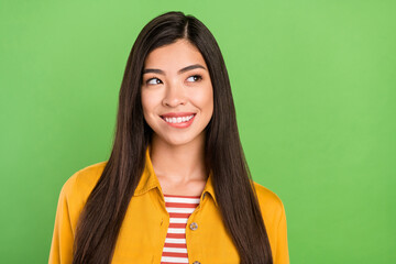 Photo of cheerful pretty young woman look empty space bite lip teeth creative isolated on green...