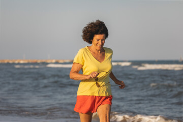 Fototapeta na wymiar A cheerful and vital woman, in her 70s, walks and runs on a beach at sunset, on the shores of the Mediterranean Sea, Spain