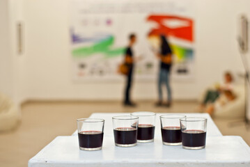 Glasses with wine on the background of the exhibition of paintings. People blurred in the background. Art salon with white walls.