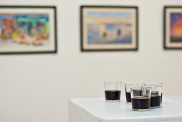 Glasses with wine on the background of the exhibition of paintings. Artwork blurred in the background. Art salon with white walls.