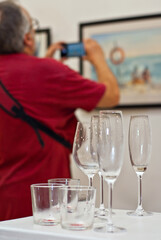 Empty wine glasses on the background of the exhibition of paintings. Artwork blurred in the background. Art salon with white walls.