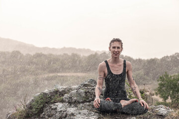 Woman doing yoga in the mountains in the evening under the rain laughs, general plan, frontal...