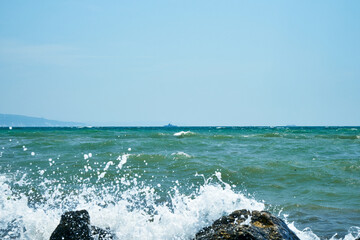 Image of the sea shore. In the background is a warship.