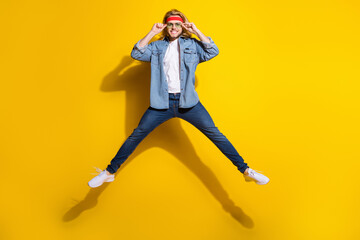 Fototapeta na wymiar Photo of pretty handsome young guy dressed denim shirt smiling arms dark eyewear jumping high isolated yellow color background