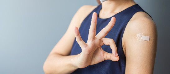 Happy woman showing OK sign with bandage after receiving covid 19 vaccine. Vaccination, herd immunity, side effect, efficiency, vaccine passport and Coronavirus pandemic