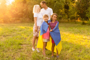 Fototapeta premium Flag Ukraine in hands of little girl in field. Child carries fluttering blue and yellow flag of Ukraine against background field.