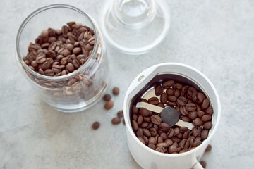 Coffee grinder with bean of coffee and a glass container with beans on a white stone table