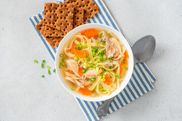 Noodle soup. Homemade soup with chicken broth, carrots and noodles in a bowl on a gray concrete background top view. Free space for text. Delicious autumn or winter soup.