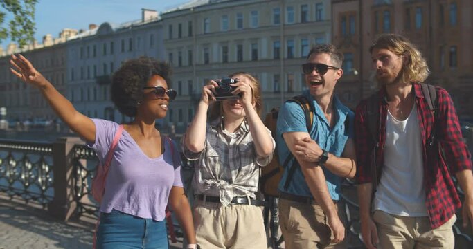 Slider shot of group of diverse friends tourists walking on city embankment