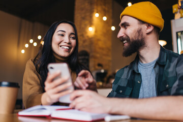 Cheerful male and female colleagues in trendy clothing enjoying communication for discussing funny publication from social networks, prosperous university friends spending time for learning together