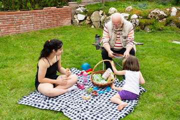 The girls are having a picnic with their grandparents. The old man is sitting on the chair.