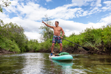 Adventurous Hispanic Adult Athletic Man paddle boarding on The River of Golden Dreams. Located in...