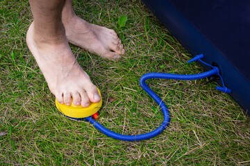 Male legs swing the inflatable mattress using a foot pump. A man stands barefoot on the grass and...