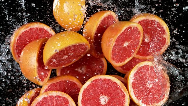 Super slow motion of sliced fresh grapefruits with water splash flying in the air. Filmed on high speed cinema camera, 1000 fps.