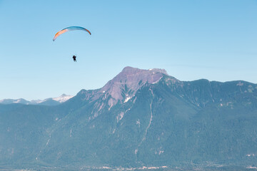Fototapeta na wymiar Adventure Composite Image of Paraglider Flying up high in the Rocky Mountains. Sunny Blue Sky. Aerial Background from Fraser Valley, British Columbia, Canada. Extreme Sport Concept