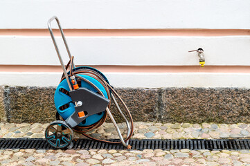 A portable garden hose in a blue reel with wheels for watering lawn, flowers and other plants.