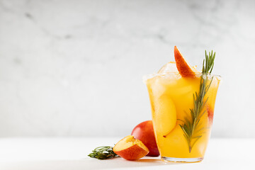 Bright fruit summer beverage with ripe peach, ice, green rosemary twig, sugar rim, fruit pieces,...