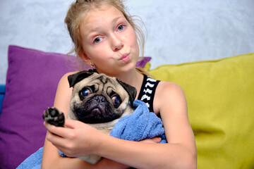 A little girl holds a pug dog wrapped in a towel