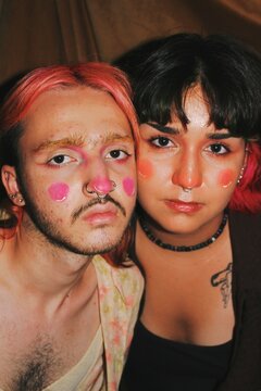 Artistic portrait of queer young nonbinary couple & friends with full face makeup and septum piercing in flash at night