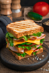A large sandwich with ham, cheese, tomatoes and cucumber close-up. Side view. Fast food.