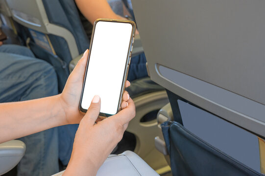 Woman Using mockup Mobile Phone While Sitting In Airplane. Woman using smartphone in airplane during flight. Mockup image of a hand holding a black mobile phone with blank desktop screen