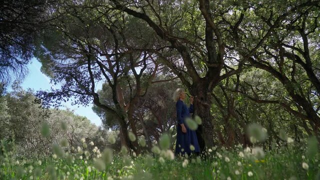 A European woman, middle-aged in a dress, walks on a prak with tall grass. With a philosophical romantic mood. Slow motion