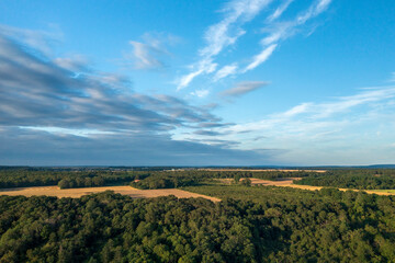 Fototapeta na wymiar Campagne entre champs et bois sous un ciel nuageux.